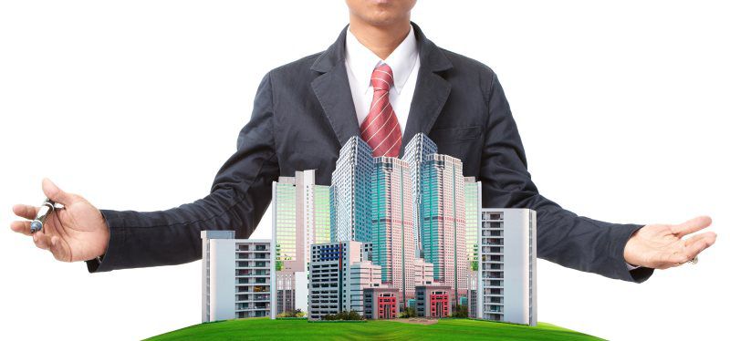 man in a suit with arms open around a miniaturized city skyline standing against a white backdrop